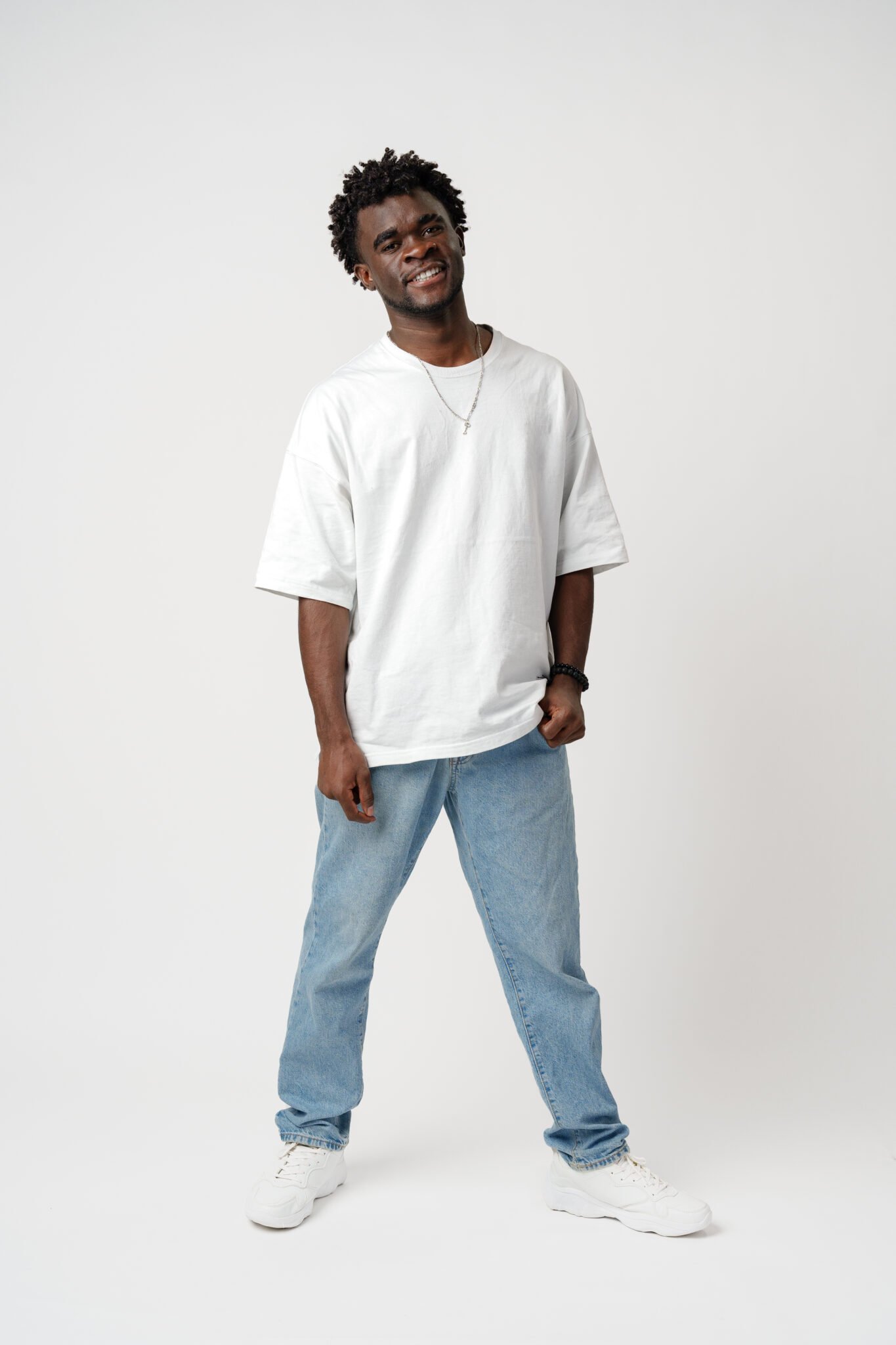 Portrait of a smiling young african man wearing white t-shirt standing over gray background in studio