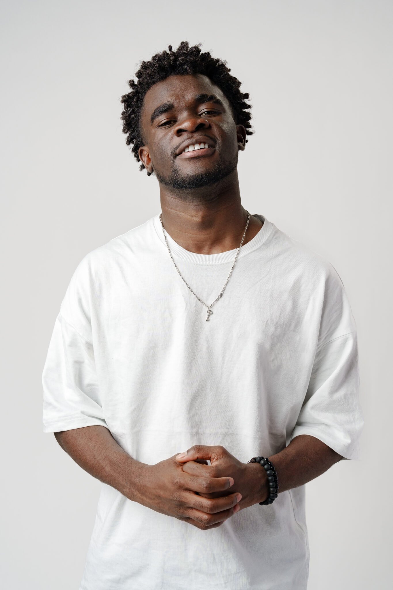 Portrait of a smiling young african man wearing white t-shirt standing over gray background in studio